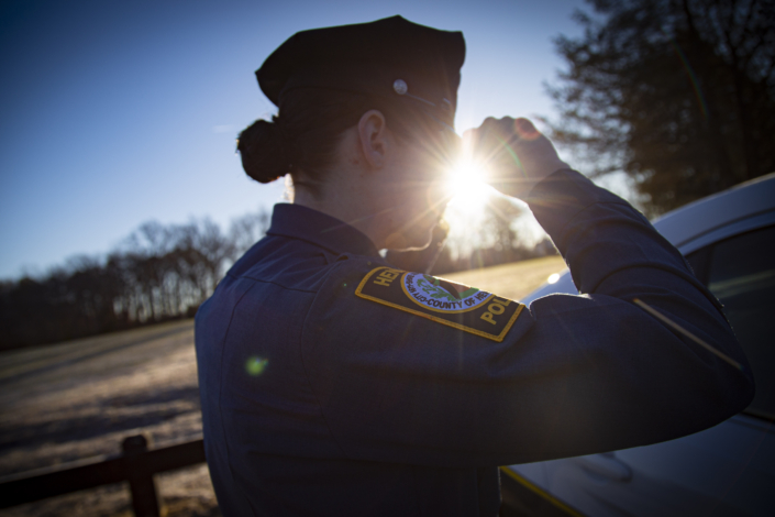 HCPD Patrol Officer Henrico Police Officer putting dress hat on in the reflection of her patrol vehicle